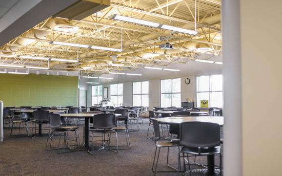 An empty cafeteria with large windows and many tables and chairs